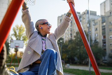 Cheerful woman with bald head hanging from metal bars at park