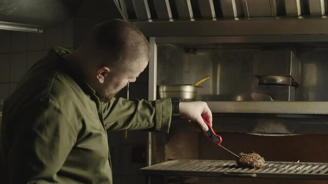 Chef prepares bbq steak in restaurant kitchen. The cook checks the doneness of the meat with a thermometer. High quality 4k footage