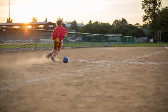 Boy kicking soccer ball on empty baseball field at dusk
