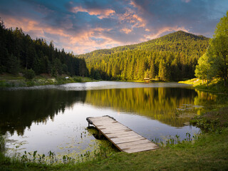 Sunset time on a beautiful forest lake. Wooden empty pier on the lake
