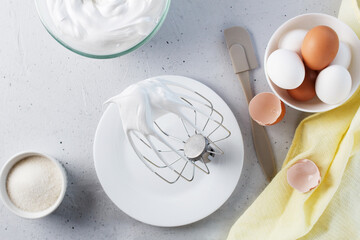 Whipped egg whites - whipped Italian meringue on a wire whisk, eggs, sugar, on a gray background.