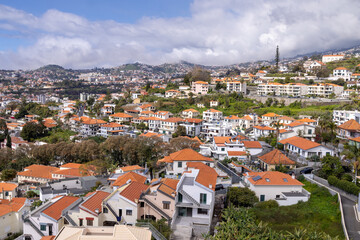 The beautiful town of Funchal in Madeira Island in Portugal showing typical Portuguese houses on a sunny summers day with clouds in the sky over the mountains.