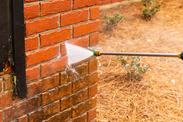 Dirty brick wall being cleaned with a pressure washer.