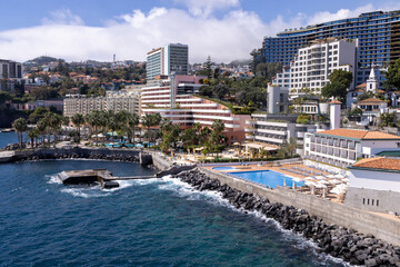 Fototapeta na wymiar The beautiful town of Funchal in Madeira Island in Portugal showing typical Portuguese hotels and swimming pool, located by the ocean on a sunny summers day in the summer time.