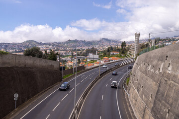 The town of Funchal in Madeira Island in Portugal showing the highway with traffic driving on the road, with the housing estate in the background, on a bright sunny summers day