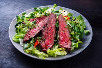 Traditional barbecue bavette beef steak slices with lambs salad and iceberg lettuce served as close-up on a design plate