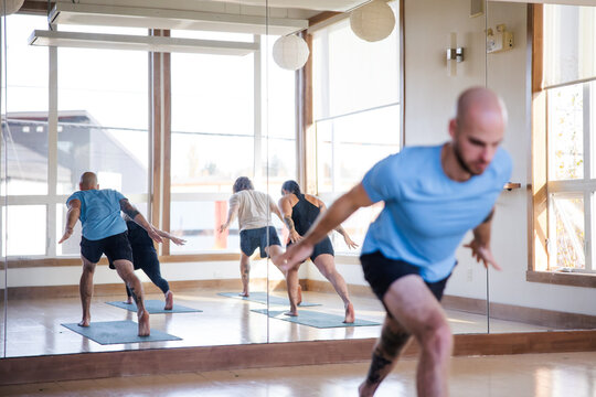 Group yoga studio class in warrior flow poses.