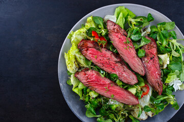 Traditional barbecue bavette beef steak slices with lambs salad and iceberg lettuce served as top view on a design plate with copy space left