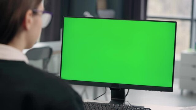 Young Girl Working At Computer With Green Mock Up Screen in Office. Close Up Desktop Computer Monitor with Mock Up Green Screen Chroma Key Display