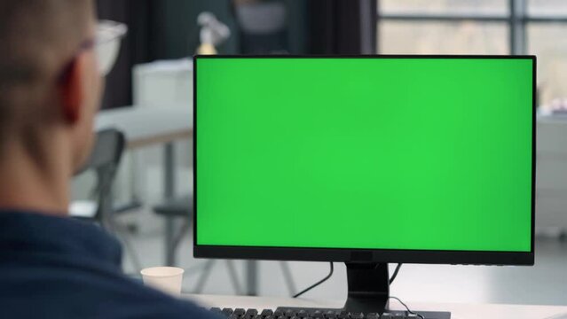 Young Man Working At Computer With Green Mock Up Screen in Office. Close Up Desktop Computer Monitor with Mock Up Green Screen Chroma Key Display