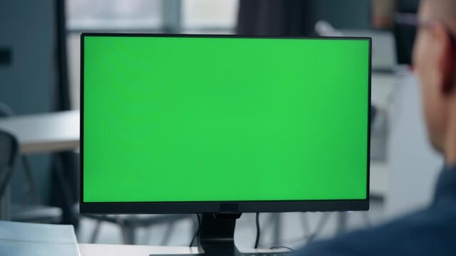 Young Man Working At Computer With Green Mock Up Screen in Office. Close Up Desktop Computer Monitor with Mock Up Green Screen Chroma Key Display