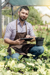 Man-gardener with tablet and plant in garden center