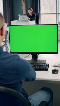 Young Man Working At Computer With Green Mock Up Screen in Office. Close Up Desktop Computer Monitor with Mock Up Green Screen Chroma Key Display. Vertical Video