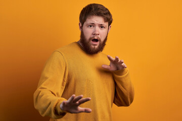 Body language concept. Frightened man with fearful expression, gestures with palms, makes defense sign, exlaims with astonished expression, dressed in red casual t shirt isolated.