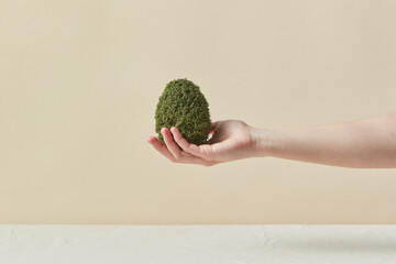 Handmade green mossy Easter egg in woman's hand.