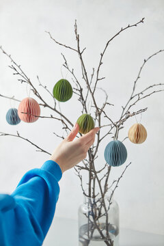 Paper Easter eggs hung on branches by woman.