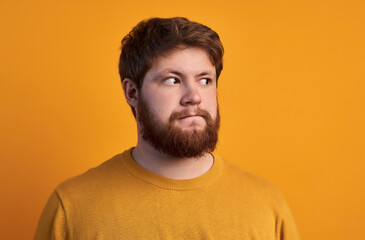 Doubtful hesitant male with ginger hair and beard, closes one eye and looks with clueless...