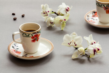 Obraz na płótnie Canvas Espresso coffee in Italian porcelain cup with floral pattern. Orchid flowers around.