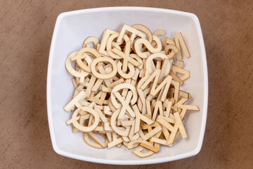 Top view of a white plate full of small wooden letters on a wooden background