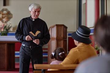Senior priest standing with Bible reading sermon for people in the church