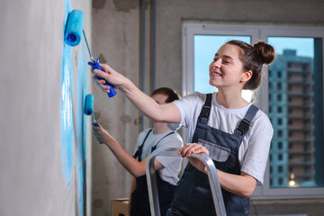 Couple in new home during repair works painting wall together. Happy family holding paint roller...