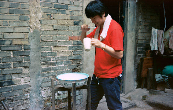 The man in red is brushing his teeth outside