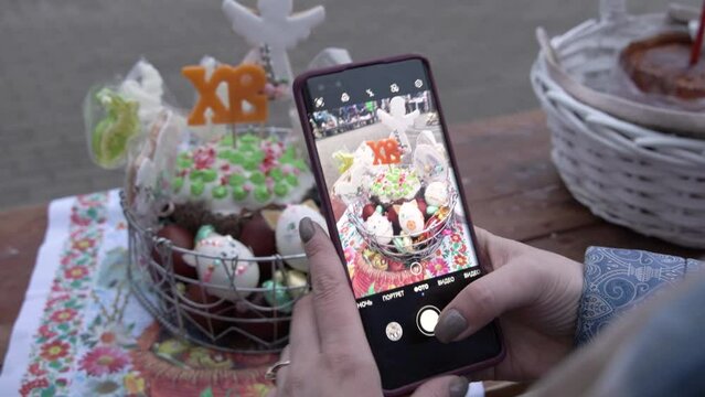 A girl takes a picture of an Orthodox Easter basket with eggs and a cupcake