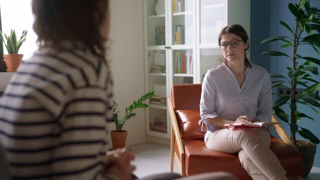 Adult woman of psychologist sitting in armchair and carefully listening attentively to anxious client during counseling session. Patient shares his mental health problems on psychologist appointment