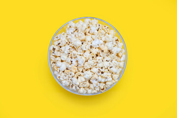 Popcorn in a large glass bowl on a yellow background, top view. Crispy classic popcorn snack for watching movies and series. Delicious light snack for watching TV