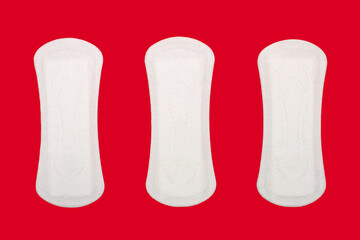 Three feminine hygiene menstrual pads are located on a red background. Feminine hygiene product in the form of sanitary pads. Clean menstrual pads ready to use. Women's daily sanitary napkins