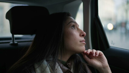 One pensive young woman sitting in car backseat looking out window. Thoughtful expression of a female passenger riding taxi