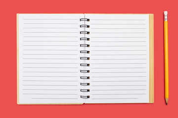 An open notebook with a binding and a yellow pencil on a red background. Open notepad with blank sheets in top view. Free space for text. Blank notebook pages ready to be used in design