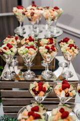 Glass glasses with a variety of cut fruits on a tray in a restaurant. Raspberry, pineapple and melon as a fruit plate for dessert in a restaurant. Delicious and healthy food