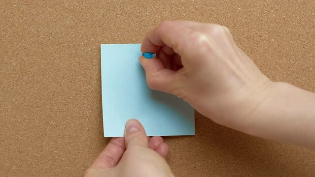 A woman's hand pins a blank paper note on a cork board. Post reminder. A place to write an idea.