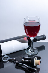 Glass with red wine next to bottle and corkscrew with cork
