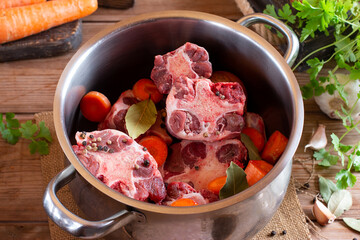 Raw veal beef Oxtail Meat with carrots, onions and spices in a saucepan on the table. Bone Broth Bouillon preparation