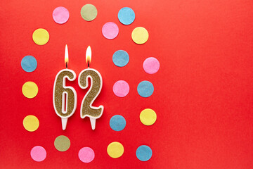 Number 62 on a red background with colored confetti. Happy birthday candles. The concept of celebrating a birthday, anniversary, important date, holiday. Copy space. banner