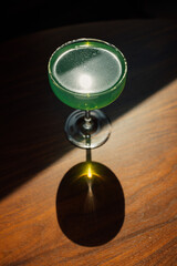 green absinthe drink in a coupe glass with on wooden table in the sun