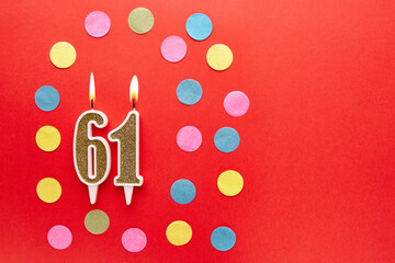 Number 61 on a red background with colored confetti. Happy birthday candles. The concept of...