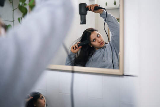 Young woman drying hair in bathroom