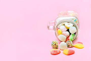 Colorful sweet different jelly candies in glass jar cup lying isolated on pink background, pastry, confectionery, desserts. Tasty delicious unhealthy colories junk food