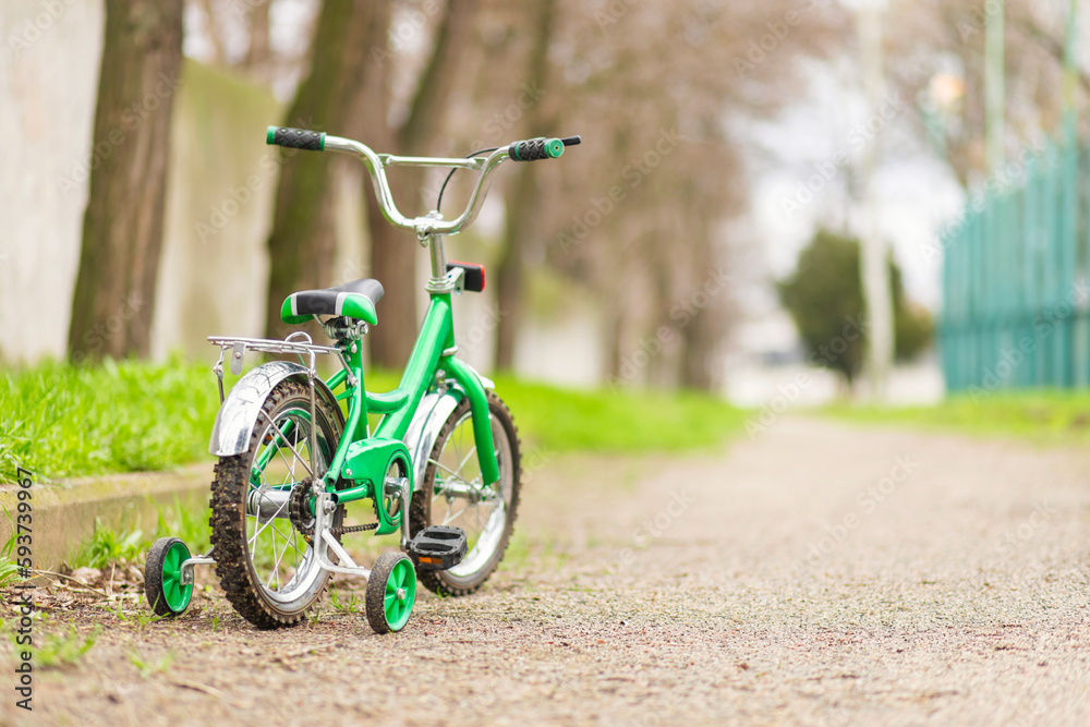 Wall mural A green bicycle for children with additional wheels at road in park