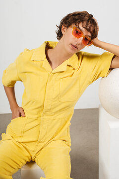 White girl with short hair and glasses wearing yellow jumpsuit