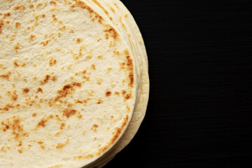 Stack of Whole Wheat Flour Tortillas on a black background, top view. Flat lay, overhead, from above. Close-up.