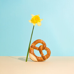 Bread bagel in heart shape with sesame seeds and yellow narcissus on sky blue background. Minimal...