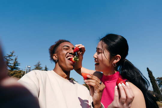 Funny selfie of multiracial couple eating strawberries