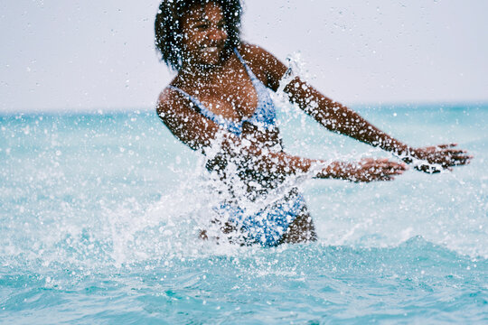 Cheerful black woman splashing water in sea