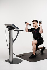 Muscular male athlete in EMS suit is doing workout sport training that uses electrical impulses to...