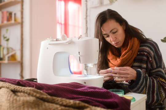 Focused woman sewing clothes at home