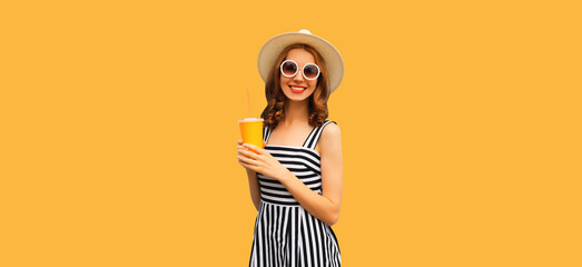 Summer portrait of happy smiling young woman drinking fresh fruit juice wearing straw round hat, striped dress on orange background